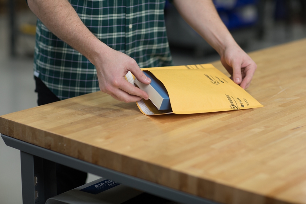man in plaid shirt packing pregis paper mailer at wooden table
